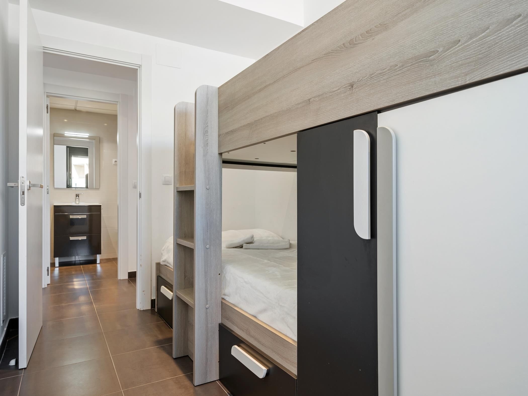 A modern, compact room with a bunk bed, a small bathroom with a mirror, and a wardrobe.