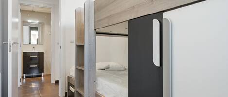 A modern, compact room with a bunk bed, a small bathroom with a mirror, and a wardrobe.