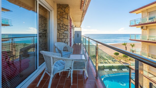 Ein Balkon mit Korbmöbeln, einer Steinmauer und Blick auf das Meer.