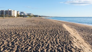 Ein weiter Sandstrand mit Fußabdrücken, einem klaren, blauen Himmel und Gebäuden im Hintergrund.
