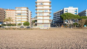 Ein Strandhotel mit mehreren Etagen, Balkonen und einem sandigen Strand im Vordergrund.