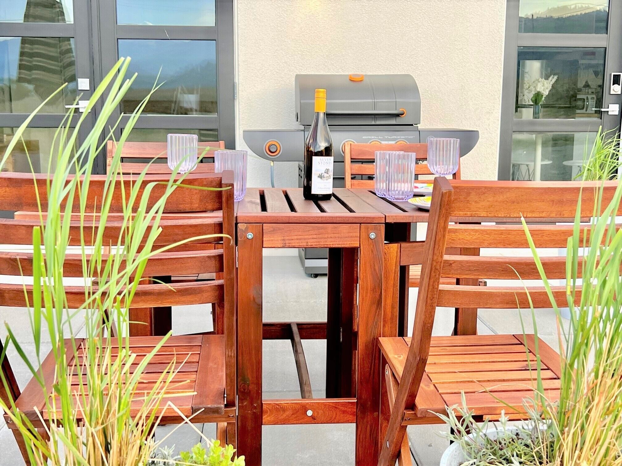 Et træbord med stole, grill og en flaske vin.