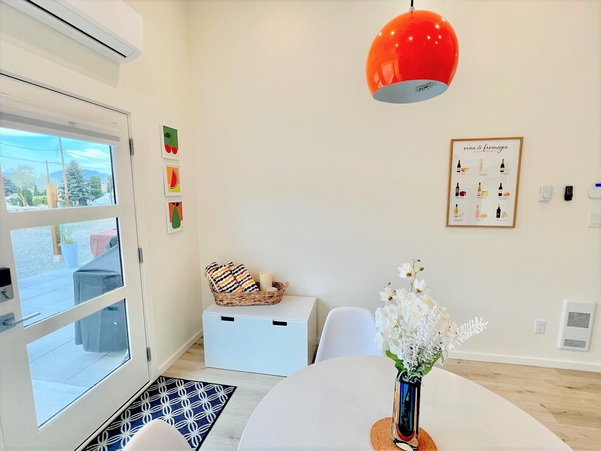 Een moderne kamer met een groot raam, een rode hanglamp, een witte tafel en een kaas- en wijnbord in een lijst.
