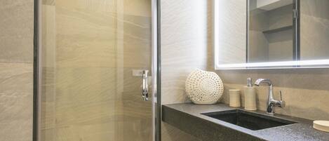 A modern bathroom with a glass shower enclosure, a granite countertop, a sink with a mirror, and a decorative vase.
