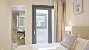 Ein Hotelzimmer mit Bett, Badezimmer mit Dusche, einem Fenster mit Vorhängen und einer Wandlampe.
