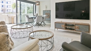 Ein modernes Wohnzimmer mit großem Flachbildfernseher, einem Essbereich mit Glastisch und einer gemütlichen Sitzecke mit Felldecke.