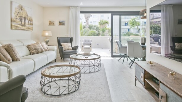 Ein modernes Wohnzimmer mit einer Couch, zwei runden Couchtischen, einer TV-Konsole und einem Balkon mit Sitzgelegenheit.