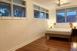 A bedroom with a wooden bed, white walls, and large windows. - Spacious Home Near CBD 20x Faster 5G @390 Mbps (Tarragindi)