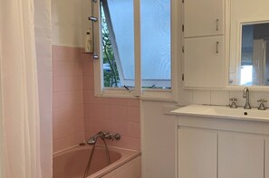 A bathroom with a bathtub, a window, and a sink with a mirror. - Spacious Home Near CBD 20x Faster 5G @390 Mbps (Tarragindi)