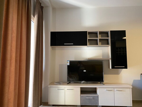 Una sala moderna con un televisor de pantalla plana sobre un mueble blanco, un centro de entretenimiento negro y una ventana con cortinas.
