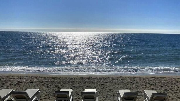 A beach with sunbathing chairs facing the ocean, clear skies, and a bright sun. - Bright and airy apartment in Puerto Banus (Marbella)