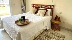 A neatly made bed with a tray of items, a bedside table with decorative objects, and a framed picture on the wall. - Bright and airy apartment in Puerto Banus (Marbella)