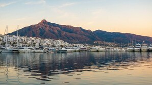 A marina with boats docked, a mountain in the background, and a coastal town with white buildings. - Bright and airy apartment in Puerto Banus (Marbella)