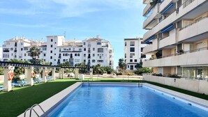 A swimming pool with a clear blue water surface, surrounded by a well-maintained lawn and lounge chairs. - Bright and airy apartment in Puerto Banus (Marbella)