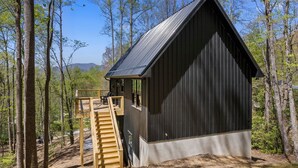 Eine Holzhütte mit einer Holzterrasse und einem Metalldach, umgeben von Bäumen.
