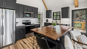 Eine moderne Küche mit dunklen Schränken, Edelstahlgeräten und einer Holztheke mit Barhocker.