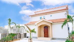 A two-story house with a red-tiled roof, a wooden door, and a small porch area. - Villa Amalfi (Miyakojima)
