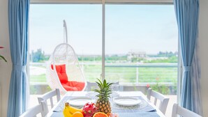 A dining table with plates, a pineapple, dragon fruit, and bananas. A hanging chair is visible in the background. - Villa Amalfi (Miyakojima)