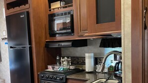 A compact kitchen with wooden cabinets, a black refrigerator, a stove, and a microwave. - Relax in Calusa Key Largo (Key Largo)
