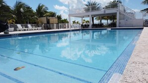 A swimming pool with clear blue water, a white deck with lounge chairs, and a covered area with stairs. - Relax in Calusa Key Largo (Key Largo)