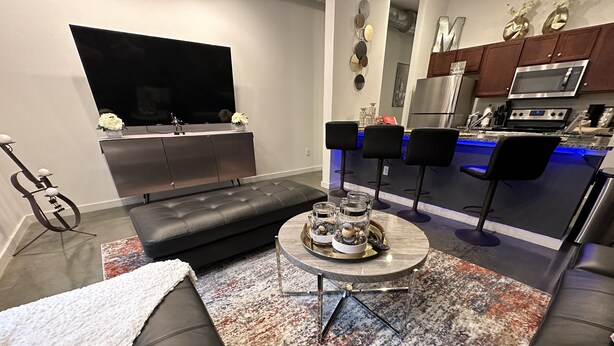 A modern living room with a black leather sofa, a flat-screen TV, a dining area with bar stools, and a kitchen with stainless steel appliances. - Honeymoon, The City of Music, king s Bed, B street (Memphis)