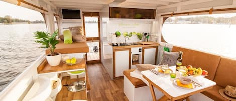Interior de embarcación compacto con zona de comedor, pequeña cocina y planta en maceta.