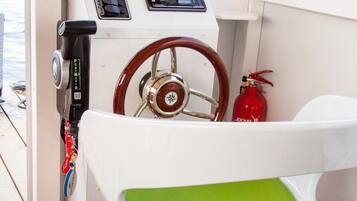 A boat's interior with a steering wheel, control panel, and a green cushioned seat.