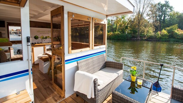 A boat interior with a dining area, a seating area with a table and chairs, and a view of the river. - Fully-Equipped Boat 'Lisa' with Terraces (Priepert)