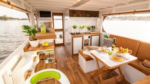 A compact boat interior with a dining area, kitchenette, and a potted plant. - Fully-Equipped Boat 'Lisa' with Terraces (Priepert)