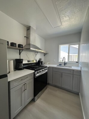 A kitchen with a stove, oven, and coffee maker. There is a window with a view of the outside.
