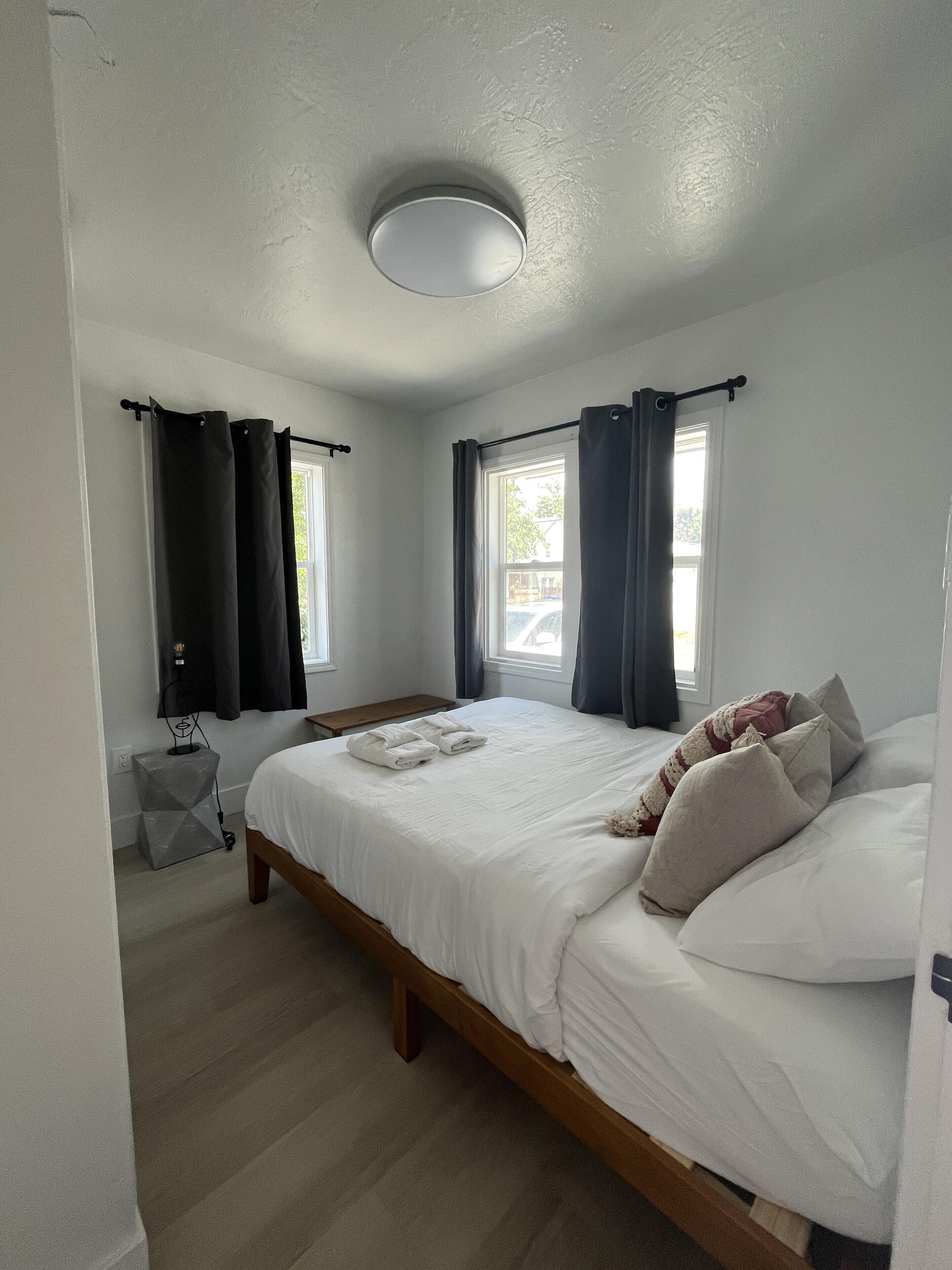 Ein Schlafzimmer mit Bett, Vorhängen, einem Fenster und einer Deckenleuchte.
