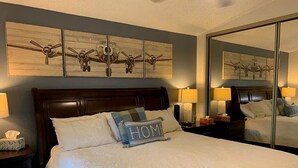 Habitación de hotel con una cama grande, dos lámparas de noche, un cabecero de madera, un espejo grande y una obra de arte en la pared sobre la cama.