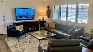 Una sala de estar con televisor de pantalla plana, sofás de cuero, una mesa de centro de vidrio y un elemento decorativo en la pared.