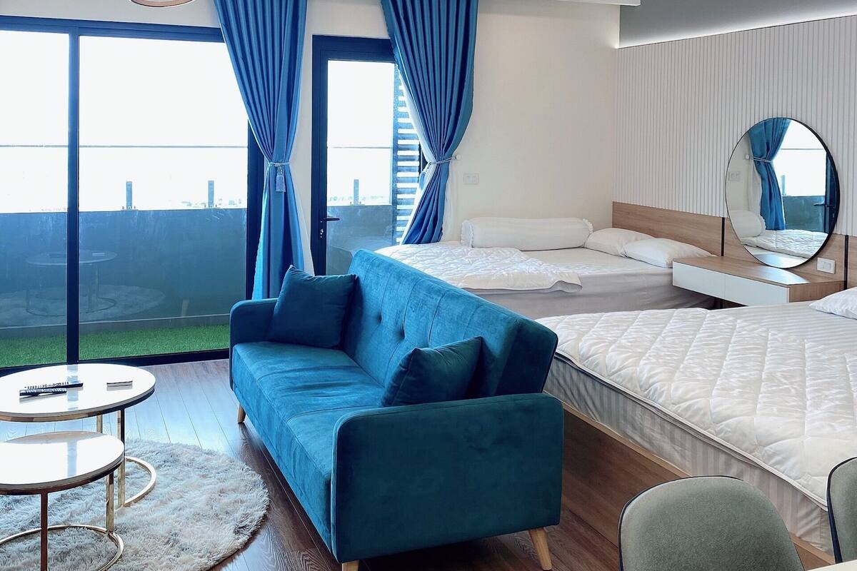 A modern hotel room with a large bed, a sofa, a round coffee table, and a view of the cityscape.