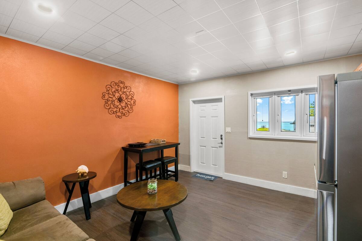 A modern kitchen with a refrigerator, a dining table with chairs, and a decorative wall piece.