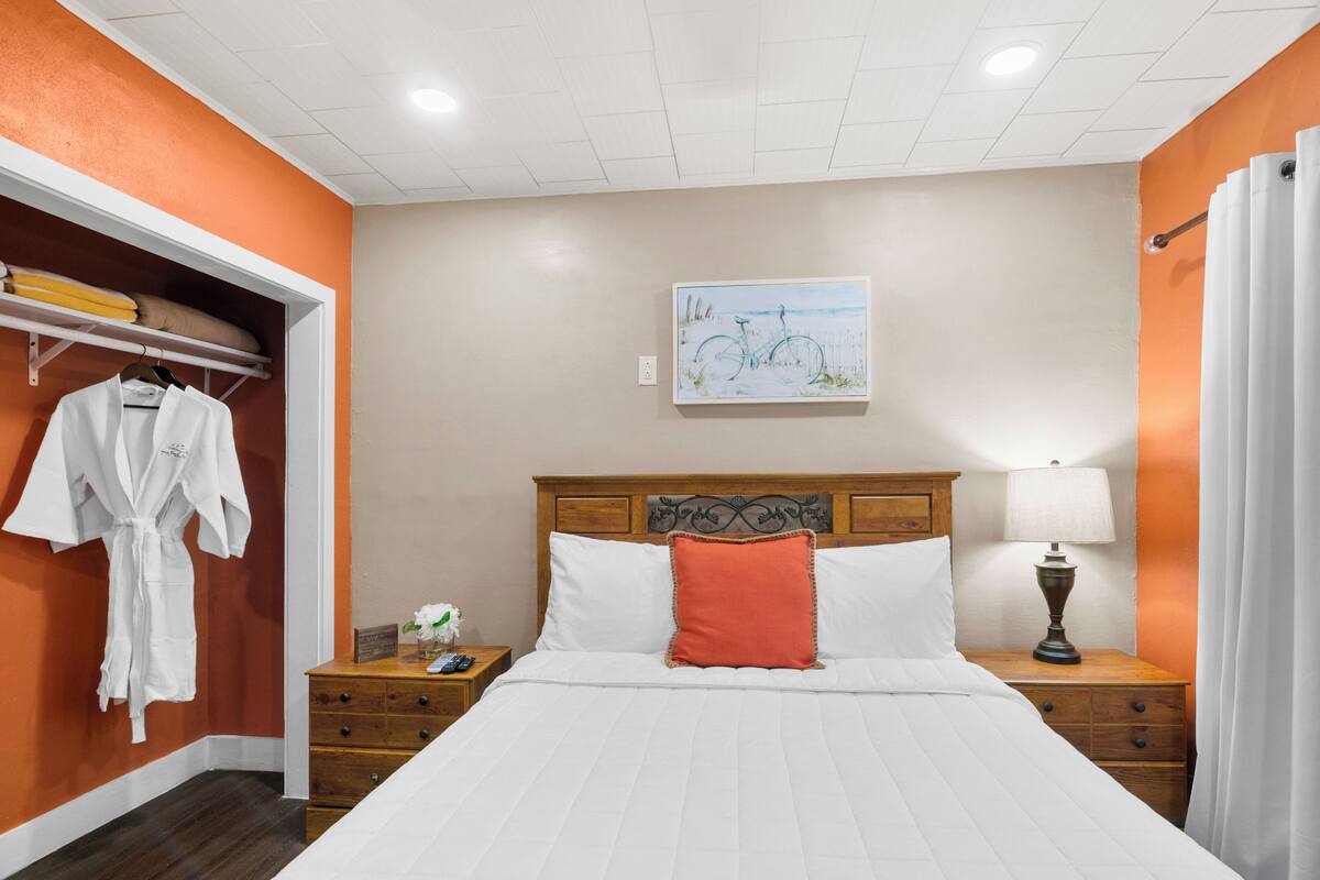 A hotel room with a bed, a nightstand, a lamp, a painting on the wall, and a robe hanging on the door.