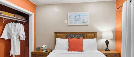 A hotel room with a bed, a nightstand, a lamp, a painting on the wall, and a robe hanging on the door.