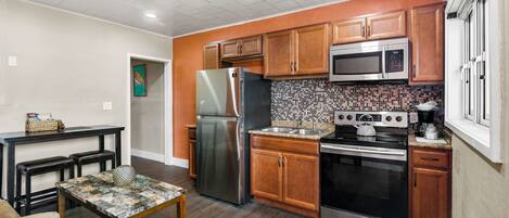 A compact kitchen with wooden cabinets, stainless steel appliances, a tiled backsplash, and a small dining area with a table and benches.