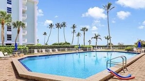 A swimming pool with a blue water slide, surrounded by palm trees and a brick walkway.