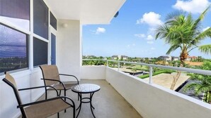 A balcony with two chairs and a small table, overlooking a residential area with palm trees and buildings.