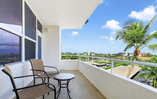 A balcony with two chairs and a small table, overlooking a residential area with palm trees and buildings. - Sunset House - Beautiful Marco Island 2/2 Beach Front Condo (Marco Island)
