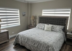 A bedroom with a large bed, two bedside tables, a nightstand, and a window with blinds. - Sunset House - Beautiful Marco Island 2/2 Beach Front Condo (Marco Island)