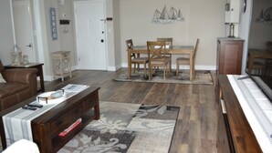 A living room with a brown leather couch, a wooden coffee table, and a dining area with a wooden table and chairs.