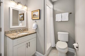 Une salle de bain avec un lavabo à dessus en granit, des toilettes blanches et un rideau de douche.