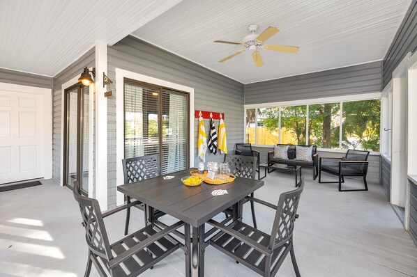 Une terrasse couverte avec une table et des chaises, un ventilateur de plafond et une vue sur l’extérieur.