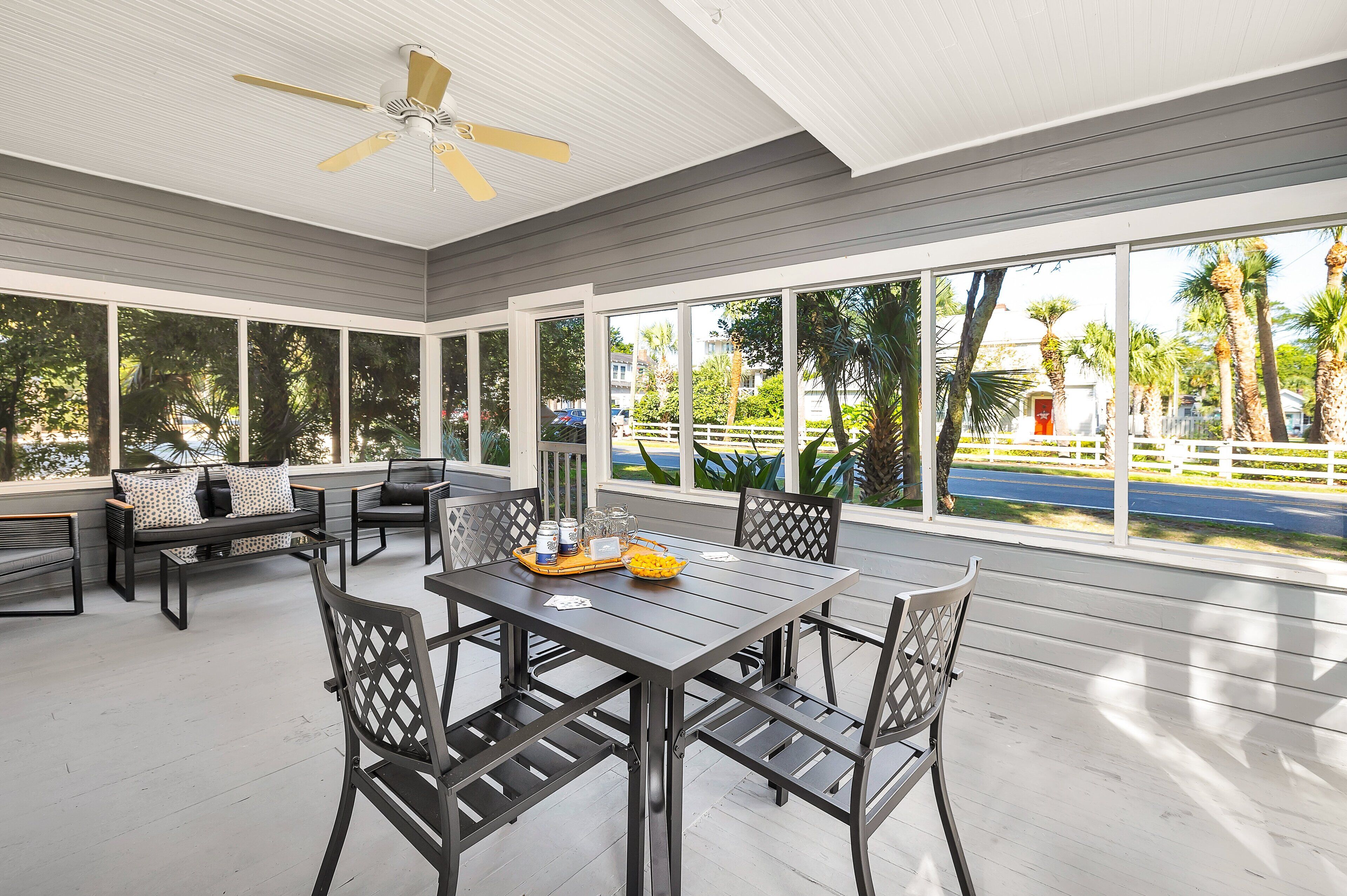 A covered patio with a table and chairs, large windows, and a ceiling fan.