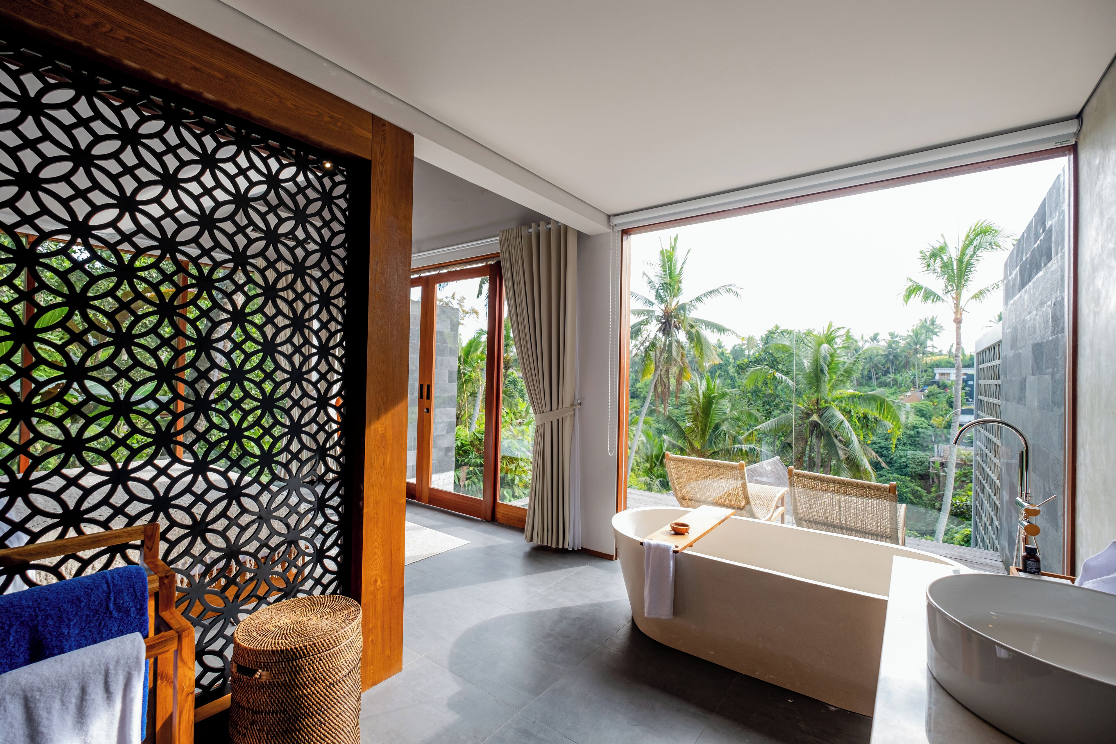 A modern bathroom with a bathtub, a large window, and a view of palm trees.
