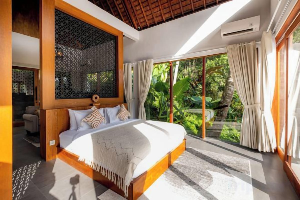 A bedroom with a large bed, a wooden headboard, and a view of greenery outside.