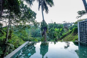 An infinity pool with a clear view of surrounding lush greenery and a palm tree. - LeRosa Valley Resort (Ubud)