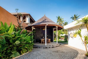 A gazebo with a tiled roof, surrounded by lush greenery and a cobblestone path.